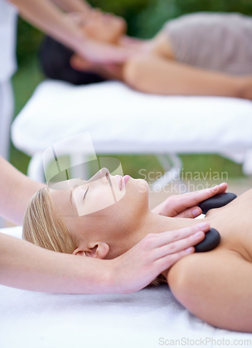 Image of Woman, zen and hot stone massage with hands of masseuse at spa, healing with holistic treatment. Rocks on shoulders, peace with therapy at wellness luxury resort, alternative medicine and self care