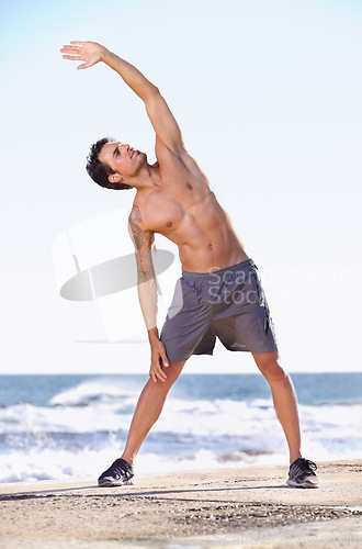 Image of Fitness, man and stretching body on beach getting ready for exercise, workout or training in nature. Fit, active or muscular male exercising in warm up stretch for healthy cardio or wellness by ocean