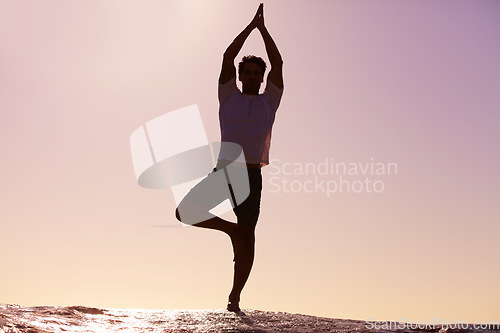 Image of Man, silhouette and yoga in sunset meditation on beach for spiritual wellness, inner peace or mental wellbeing in nature. Male yogi in tree pose for balance, healthy body or mindfulness on ocean rock