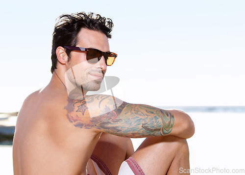 Image of Tattoo on body, young man at beach and with sunglasses sitting. Summer vacation or holiday break, freedom or traveling and happy male person relaxing at the seashore with glasses in sunshine