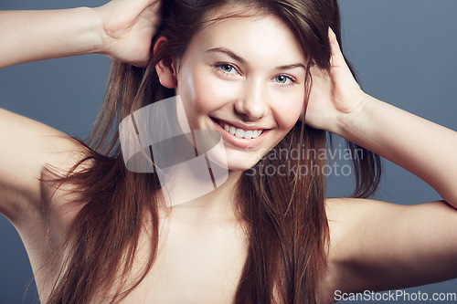 Image of Face, smile and beauty portrait of a woman in studio with natural makeup, hands in hair care and cosmetics. Headshot of aesthetic female model on a blue background for glow, skincare or facial health