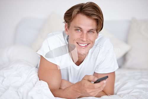 Image of Man, portrait and watching tv on a bedroom bed with happiness and remote in the morning. Happy, smile and young male person with series and movie with digital control in a house with television