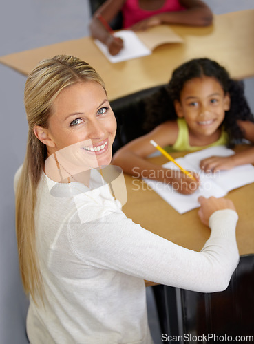 Image of Kid, teacher and portrait in classroom studying school work for an education with support. Woman, smile and desk with child to help with reading or learning for children to work at school building.