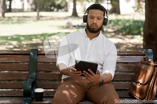 Image of Business man, headphones and outdoor with a tablet on a park bench for a break with internet. Male digital nomad and person in nature while streaming and listening to music on a audio app to relax