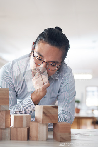 Image of Man in startup with building blocks, thinking of vision, games and design innovation for office or construction. Engineering, architecture and Asian designer with wood block for problem solving game.