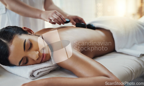 Image of Woman, hands and sleeping for rock massage, skincare or relaxation on bed at indoor beauty spa. Hand of masseuse applying hot rocks to female in relax for physical therapy or back treatment at resort