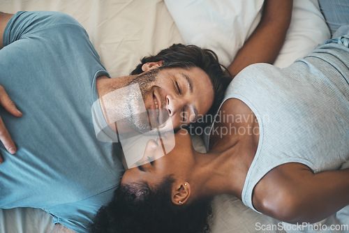 Image of Interracial couple, kiss and relax on bed above for morning bonding, intimate relationship or love at home. Top view of woman kissing man while lying in bedroom for loving romance, care or affection