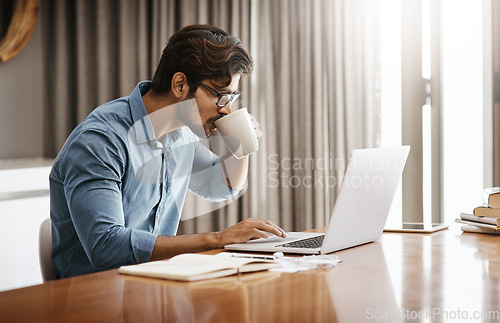 Image of Man, remote work and drinking coffee at laptop in home at table for planning, research and online network. Focused male freelancer drink cup of tea while working on computer, internet and website