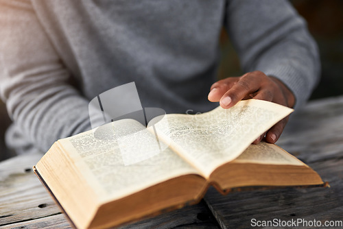 Image of Hands, book and a man reading the bible at a table outdoor for faith or belief in god closeup. Religion, story and spiritual with a male christian sitting down to read for learning or worship