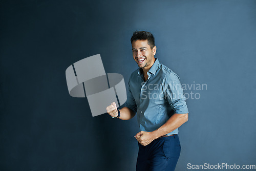 Image of Celebration, fist pump and portrait of a businessman in a studio with achievement or winning. Happy, smile and professional male employee winner with success to celebrate isolated by blue background.