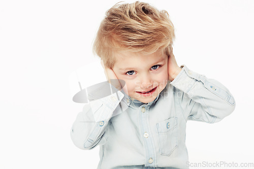 Image of Kid, happy and cover ears in portrait with shirt in studio background with cute face. Young child with smile hear loud noise while sensitive to sound in childhood as emoji on white, isolated backdrop