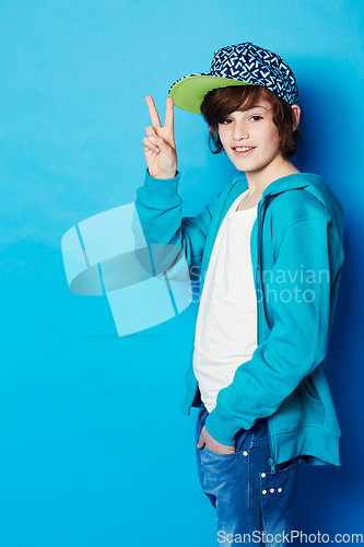 Image of Fashion, peace sign and portrait of a boy in a studio with a casual, trendy and cool outfit. Teenager, smile and happy boy kid model with hipster apparel style posing isolated by a blue background.