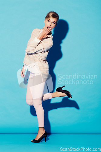 Image of Portrait, wow and gossip with a woman in studio on a blue background feeling surprised or shocked. Fashion, omg and hand on mouth with an attractive young female model looking amazed by surprise