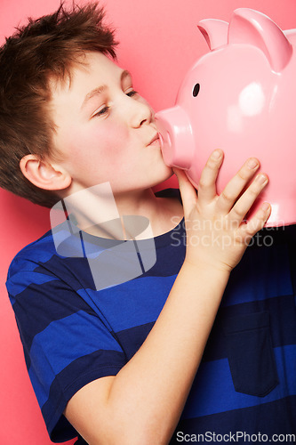 Image of Happy boy, savings and kiss on piggy bank for investment, money or coins against a pink studio background. Little child or kid holding and kissing piggybank for financial freedom, cash or growth