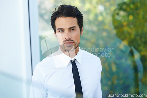 Image of Portrait, corporate and focus with a business man feeling confident in an office at work. Mindset, window or career and a handsome young male employee looking serious in his professional workplace