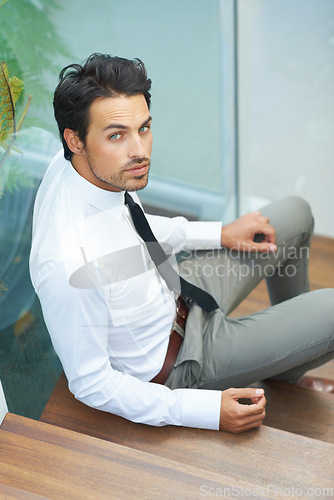 Image of Portrait, serious and stairs with a business man in a modern office at work for progress. Confidence, professional or staircase with a handsome young male employee sitting on steps in his workplace