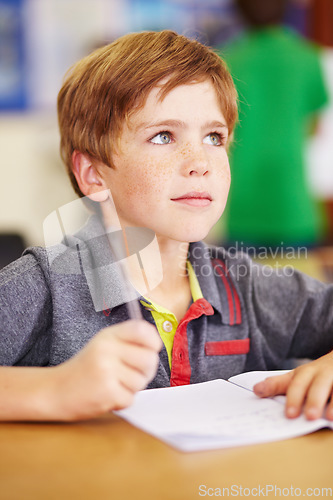 Image of School, learning and kid writing in his book while listening to lesson in the classroom. Academic, knowledge and young boy child student doing an education activity, studying or homework by her desk.