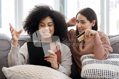 Image of Tablet, credit card and online shopping with woman friends on a sofa in the living room of their home together. Ecommerce, technology and sale with female roommates browsing for deals on the internet