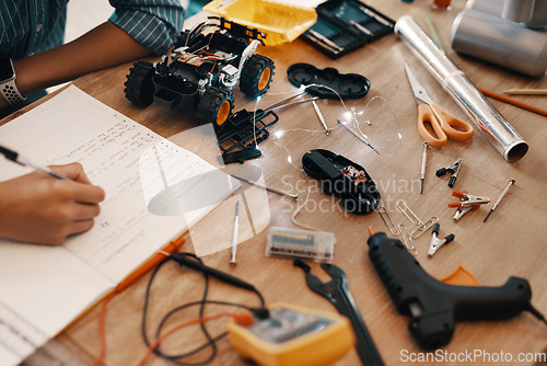 Image of Engineering, person hand with notebook for homework and stationary or robot toys on desk at home. Technology, education or creative and male child writing or research information with pen in book