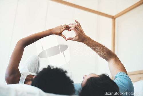 Image of Interracial couple, hands and heart emoji in bed for morning, love or care relaxing together at home. Man and woman lying in bedroom with touching hand for loving symbol, sign or gesture at the house