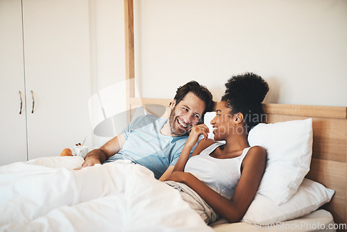 Image of Interracial couple, laughing and relax on bed for morning bonding, funny relationship or joke at home. Happy woman and man with smile, laugh and lying in bedroom for fun talk or conversation indoors