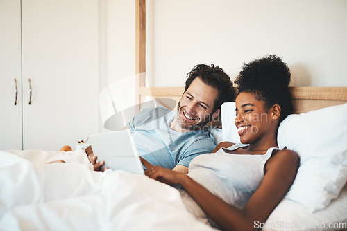 Image of Happy couple, tablet and relax on bed for morning entertainment or online streaming together at home. Interracial man and woman person relaxing in bedroom on technology for social media or browsing