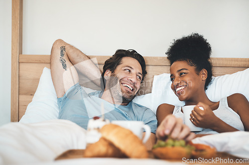 Image of Happy interracial couple, bed and breakfast in relax for morning, bonding or relationship at home. Man and woman smiling with food, coffee or meal relaxing on holiday or weekend together in bedroom