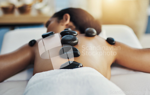 Image of Woman, relax and stone massage at spa for skincare, beauty or body treatment on bed at resort. Calm female lying in relaxation with hot rocks or pile on back in therapy, zen or wellness at salon