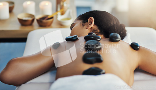 Image of Woman, relax and rock massage at spa for skincare, beauty or body treatment on bed at resort. Calm female lying in relaxation with hot rocks or stone pile on back in therapy, zen or wellness at salon