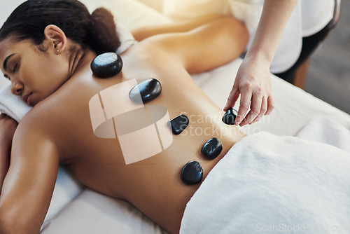 Image of Woman, hands and stone massage at spa for skincare, beauty or body treatment on bed at resort. Calm female lying in relaxation with masseuse, hot rocks and back for therapy, zen or wellness at salon