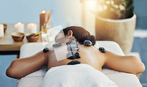 Image of Woman, relax and rock in back massage at spa for skincare, beauty or body treatment on bed at resort. Calm female lying in relaxation with hot rocks or stone pile in therapy, zen or wellness at salon