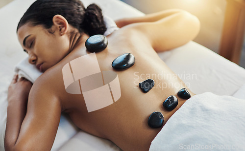 Image of Woman, sleeping and stone massage at spa for skincare, beauty or body treatment on bed at resort. Calm female lying in relaxation with hot rocks on back for physical therapy, zen or wellness at salon