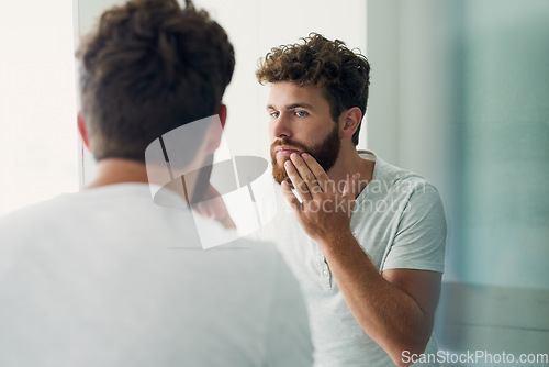 Image of Skincare, beauty and beard with a man in the bathroom of his home in the morning for fresh hygiene. Mirror, reflection and self care with a handsome young male person checking his face or skin