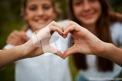 Image of Love hand sign, happy sisters in garden with fun relationship, bonding and care with siblings. Heart hands, girls and nature, kindness and friendship for teenagers in park for quality time together.