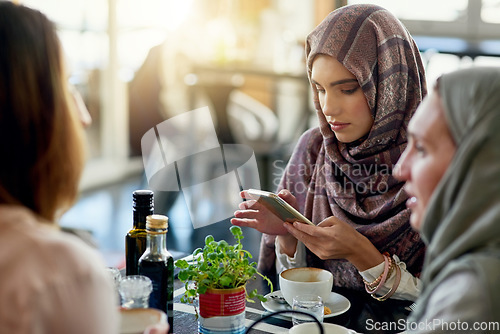 Image of Friends, phone and Muslim women in cafe, bonding and talking together. Coffee shop, cellphone and Islamic girls, group or people relax, conversation and discussion for social meeting in restaurant.