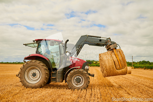 Image of Hay, agriculture and a red tractor on a farm for sustainability outdoor on an open field during the harvest season. Nature, sky and clouds with an agricultural vehicle harvesting in the countryside
