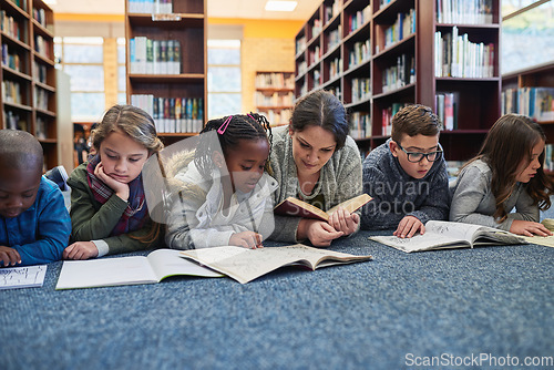 Image of Education, teacher with children in library and lying on the floor of elementary school. Studying or knowledge with books, diversity and young students with woman reading textbook or notebook.