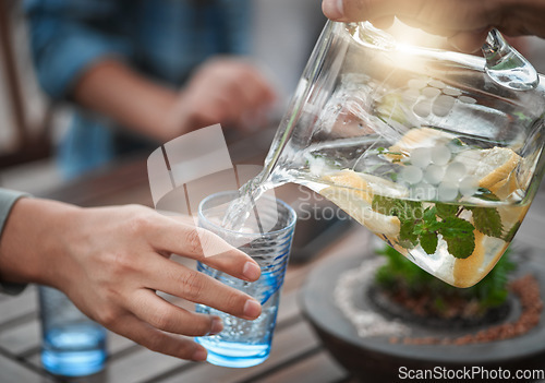 Image of Hands, closeup and water into a glass, outdoor and social gathering with friends, drink and cool down. Zoom, people and friends with clear liquid, ice and lunch with fresh mint, lemon and natural