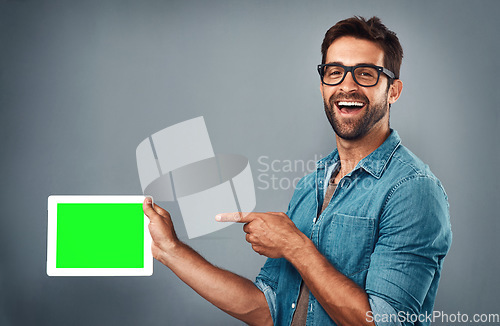 Image of Happy man, tablet and pointing on mockup green screen for advertising against a grey studio background. Portrait of male person with smile showing technology display, chromakey or copy space branding