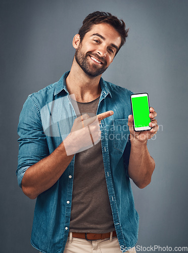 Image of Happy man, phone and pointing to mockup green screen for advertising against a grey studio background. Portrait of male person smiling and showing smartphone display or chromakey for advertisement