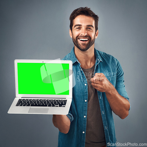 Image of Happy man, laptop and pointing with green screen in advertising or marketing against a grey studio background. Portrait of male person showing computer display, mockup or copy space for advertisement