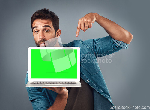 Image of Man, laptop and pointing on mockup green screen for advertising or marketing against a grey studio background. Portrait of male person showing computer display, chromakey or mock up for advertisement