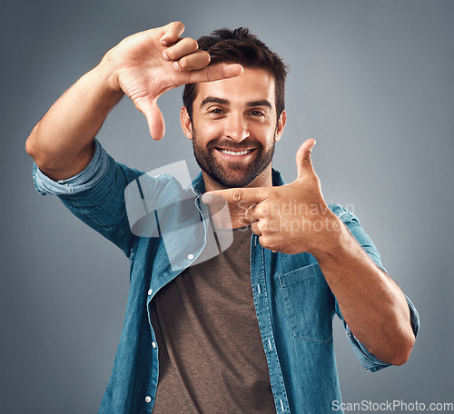 Image of Frame, face and portrait of man in studio on gray background with happiness, confident and smile. Finger border, fashion and happy male person with hand sign for picture, photography and perspective