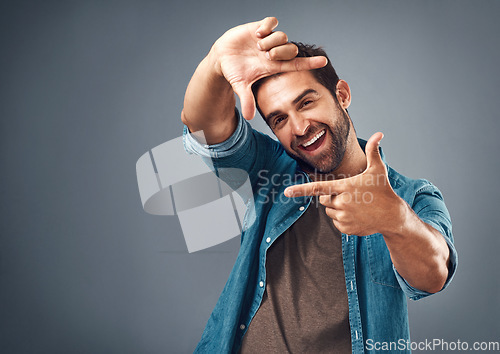 Image of Frame, excited and portrait of man in studio on gray background with happiness, confident and smile. Finger border, face and happy male person with hand sign for picture, photography and perspective