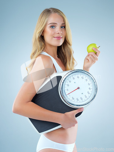 Image of Woman in portrait, apple with scale and lose weight, smile with healthy food isolated on studio background. Happy female model, health and diet with organic fruit with nutrition and weightloss