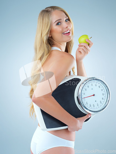 Image of Woman is eating apple, smile with scale and lose weight, portrait and healthy food isolated on studio background. Happy female model, health and diet with organic fruit with nutrition and weightloss