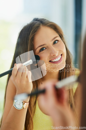 Image of Portrait, makeup and blush with a woman in the bathroom, using a mirror to apply cosmetics to her face. Reflection, brush and smile with a happy young female person applying blusher in the morning