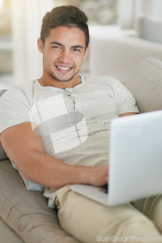 Image of Laptop, sofa and portrait of man doing remote work in his home, house or apartment with smile and relax. Couch, happy and young male person or student typing a project online, website or web