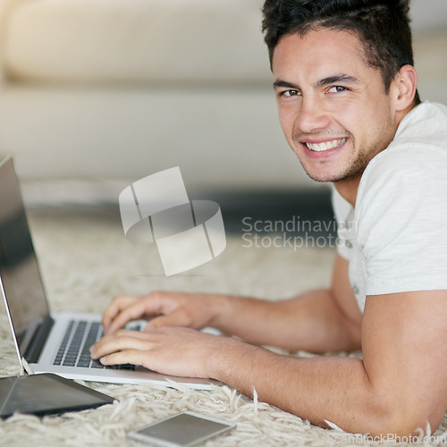 Image of Laptop, blogging and portrait of man typing as remote work in his home, house or apartment with smile on the floor. Carpet, happy and young male person or freelancer working on project online or web