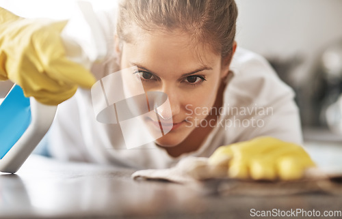 Image of Cleaning, focus and a woman wiping a table of dust or bacteria for housework. Serious, bottle and a young lady or cleaner spraying a liquid to clean a desk or counter in a house for housekeeping